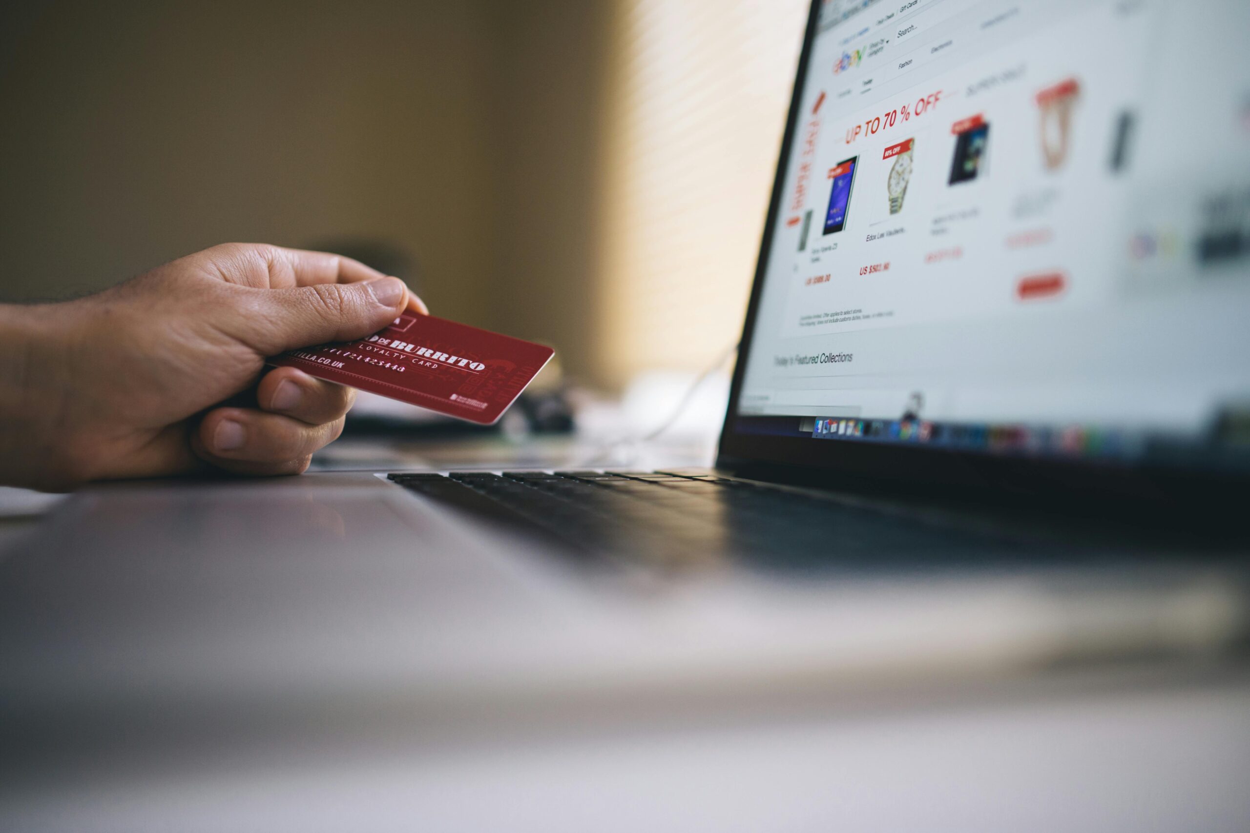 A photograph of a person holding a credit card while looking at a laptop.